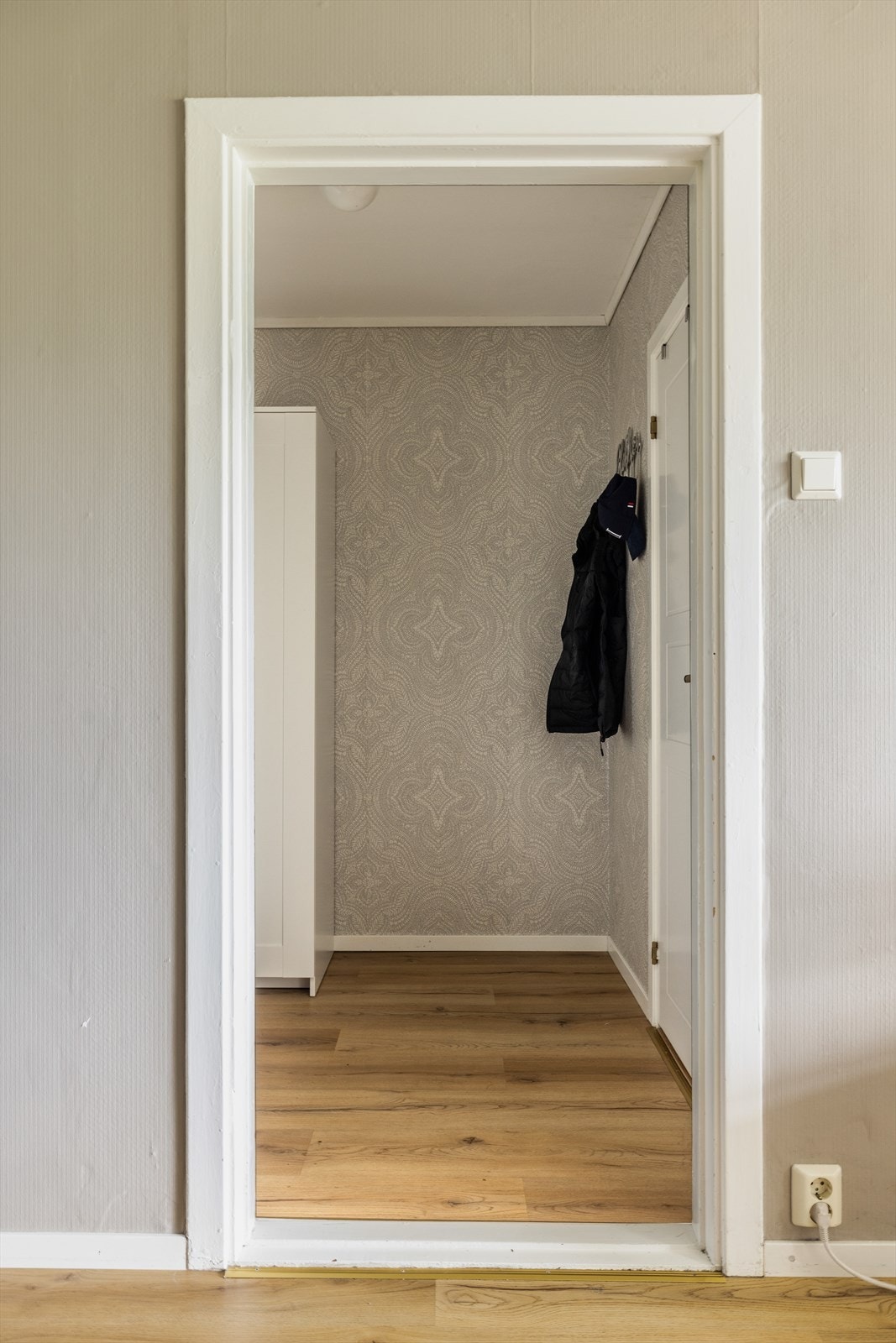 Lys og innbydende entre med laminat på gulv, tapetserte vegger og malt tak. Galleribilde