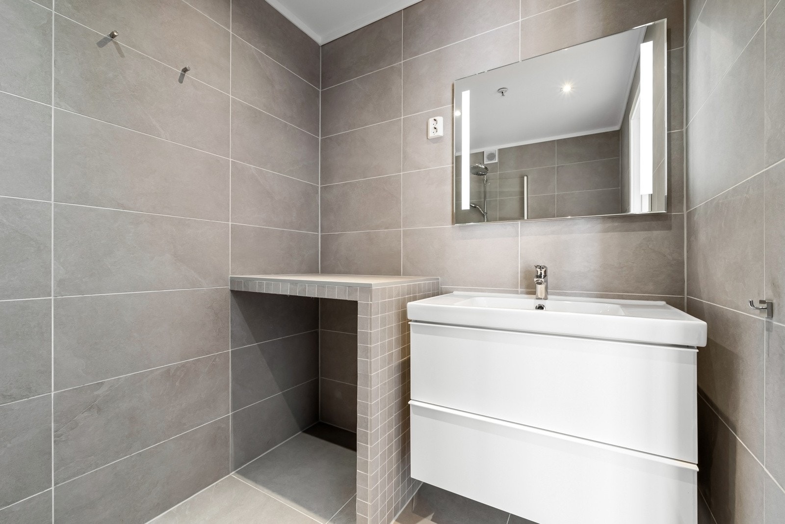 Smakfullt bad med flislagte overflater og varmekabler i gulv, nyoppusset i 2018. Innredningen består av moderne servantmøblement med 2 skuffer, speil m/integrert belysning og vegghengt toalett. Galleribilde