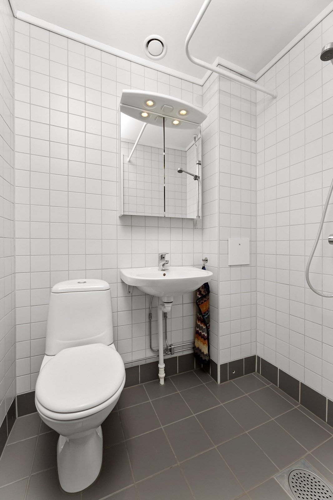 Flislagt baderom med nye varmekabler og nye gulvfliser i 2022. Badet er utstyrt med en servant med speilskap og belysning, gulvmontert toalett og dusjhjørne. Galleribilde