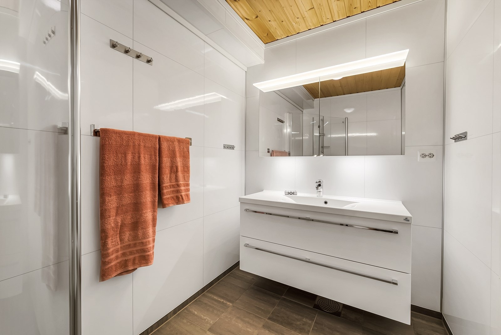 Moderne og tidløst innredet bad med baderomsplater på vegg og fliser med varmekabler på gulv. Badet er videre innredet med baderomsinnredning, toalett og dusjløsning med glassdører. Galleribilde