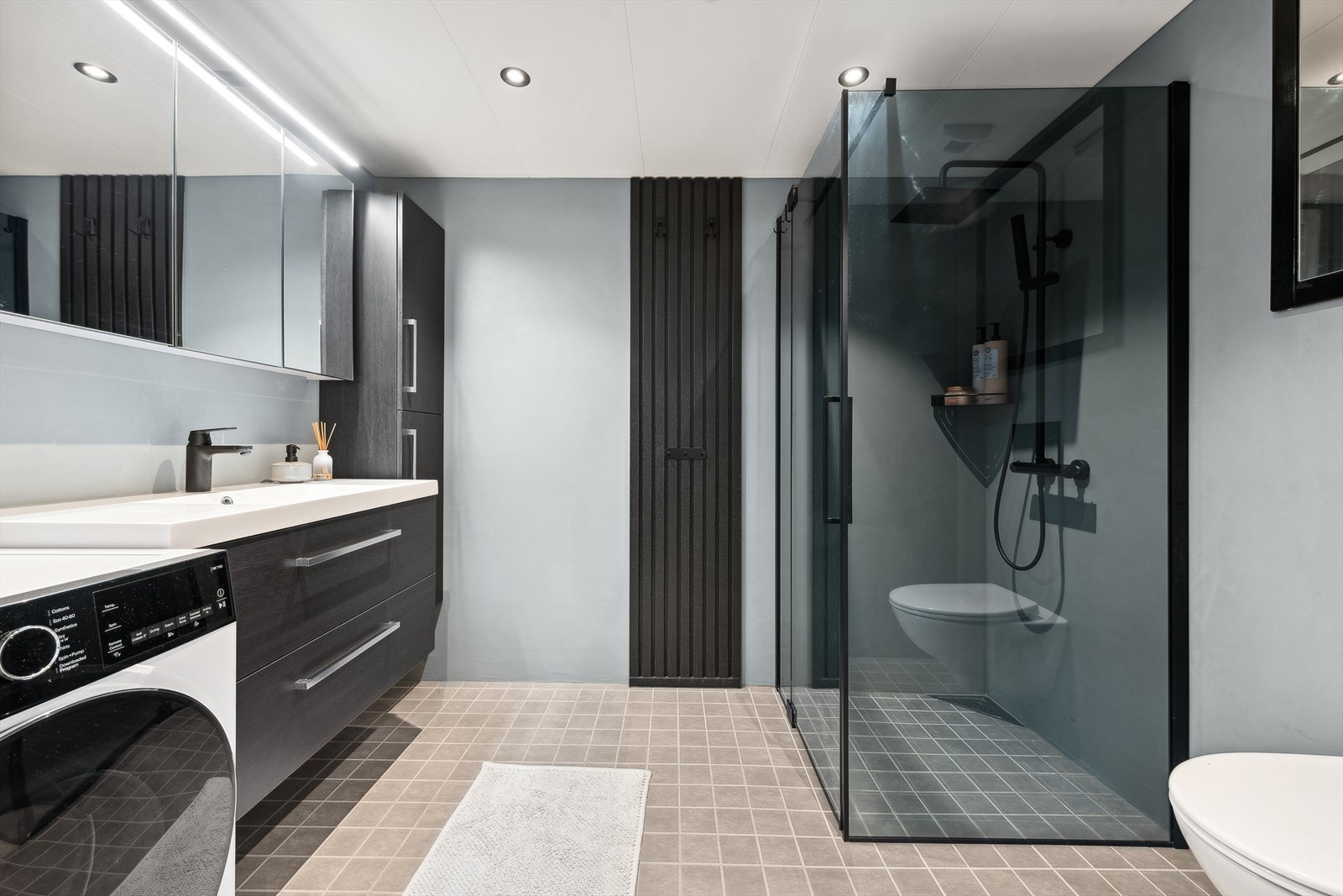 Det flislagte badet, som ble modernisert i 2023, er både delikat og funksjonelt. Veggene er dekket med mikrosement, mens stilige downlights i himlingen gir rommet et moderne og elegant preg. Galleribilde