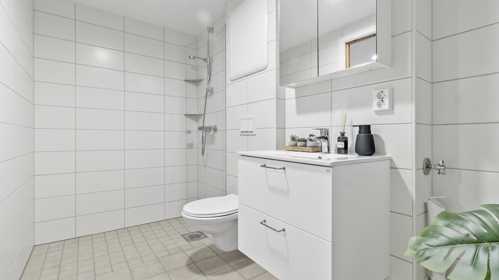 Badet er utstyrt med vegghengt toalett, helstøpt servant, skuffer under servant, dusjdører i klart glass, opplegg for vaskemaskin og fordelerskap til rørsystemet Galleribilde