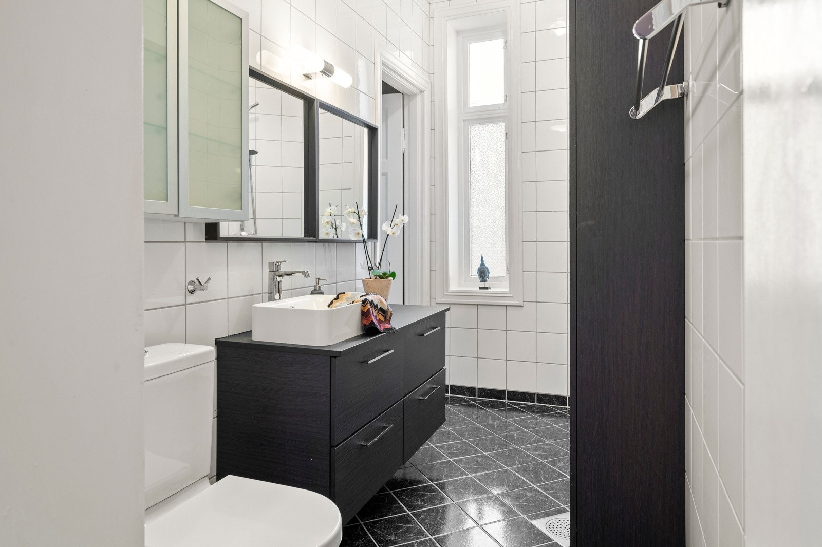 Baderomsinnredning fra 2018 med bred benkeplate, ovenpåliggende servant og stort speil med belysning over. Galleribilde