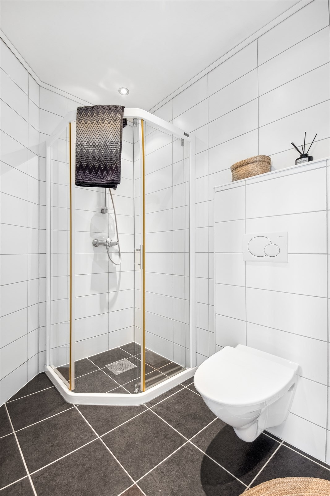 Badet er utstyrt med en innredning med toppmontert servant, speil med overliggende lys, veggmontert toalett og dusjhjørne. Galleribilde
