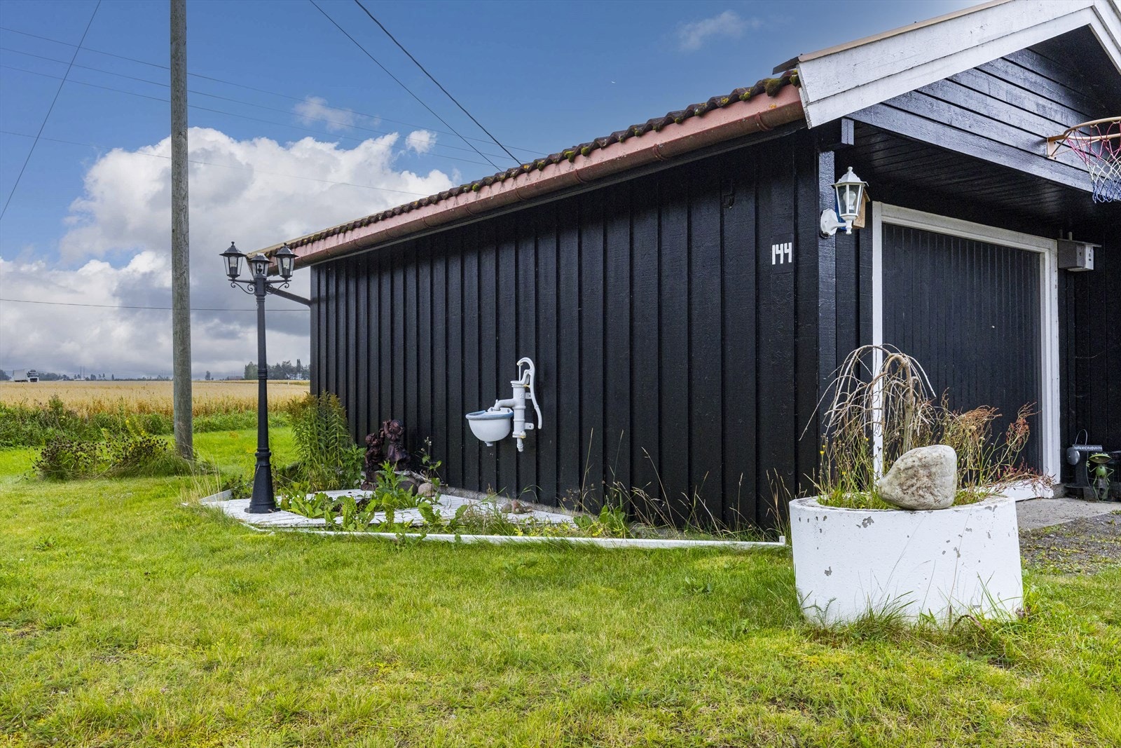 Garasjen med byggeår 1994, har gulv med støpt såle på mark med murt Leca-ringmur, utvendig stående kledningsbord, liggende kledningsbord i gavlene. Vippeport i heltre, innvendig vegger og himling med åpent bindingsverk. Galleribilde