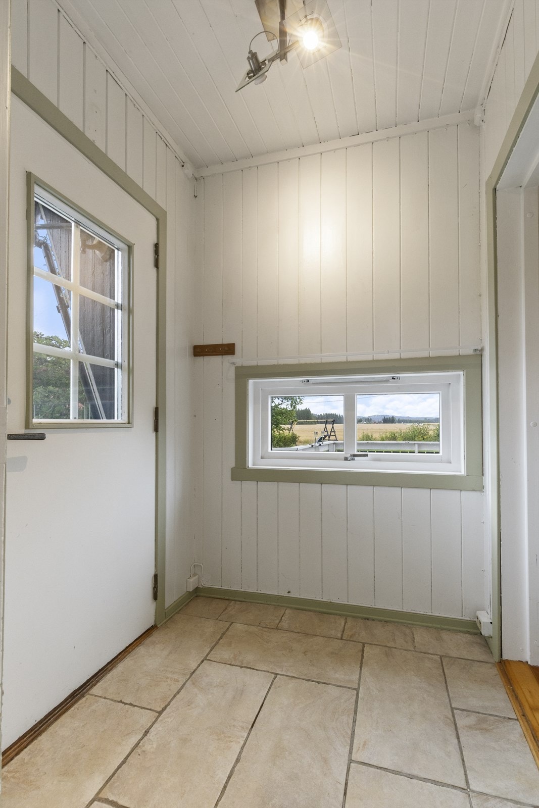 Vindfang/gang med malt panel på vegg og i himling, flis på gulv og inngang til ekstra toalettrom. Praktisk myggnetting på ytterdør. Galleribilde