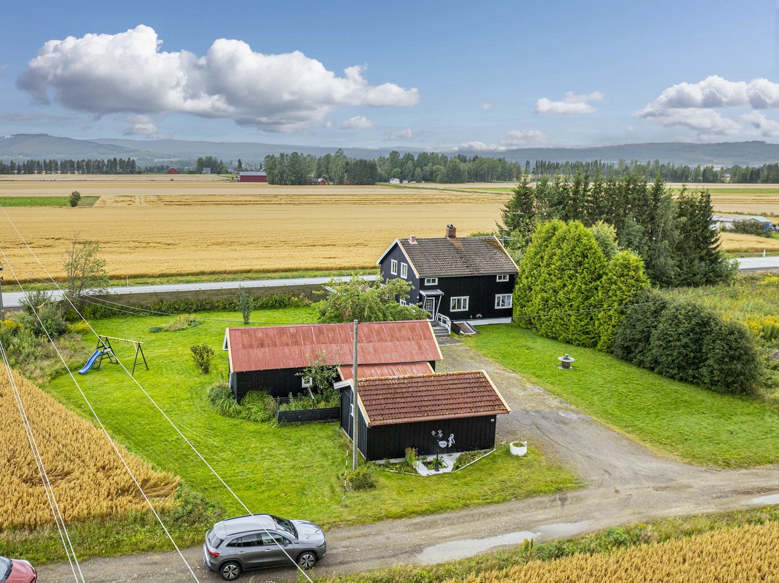 Dronefoto ved innkjørsel til eneboligen med tregrense mot tilleggs tomt, til høyre i bildet. Galleribilde