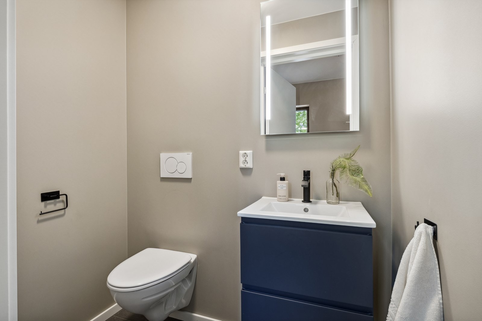 Pent gjestetoalett med servantinnredning og speil med lysskinne. Galleribilde