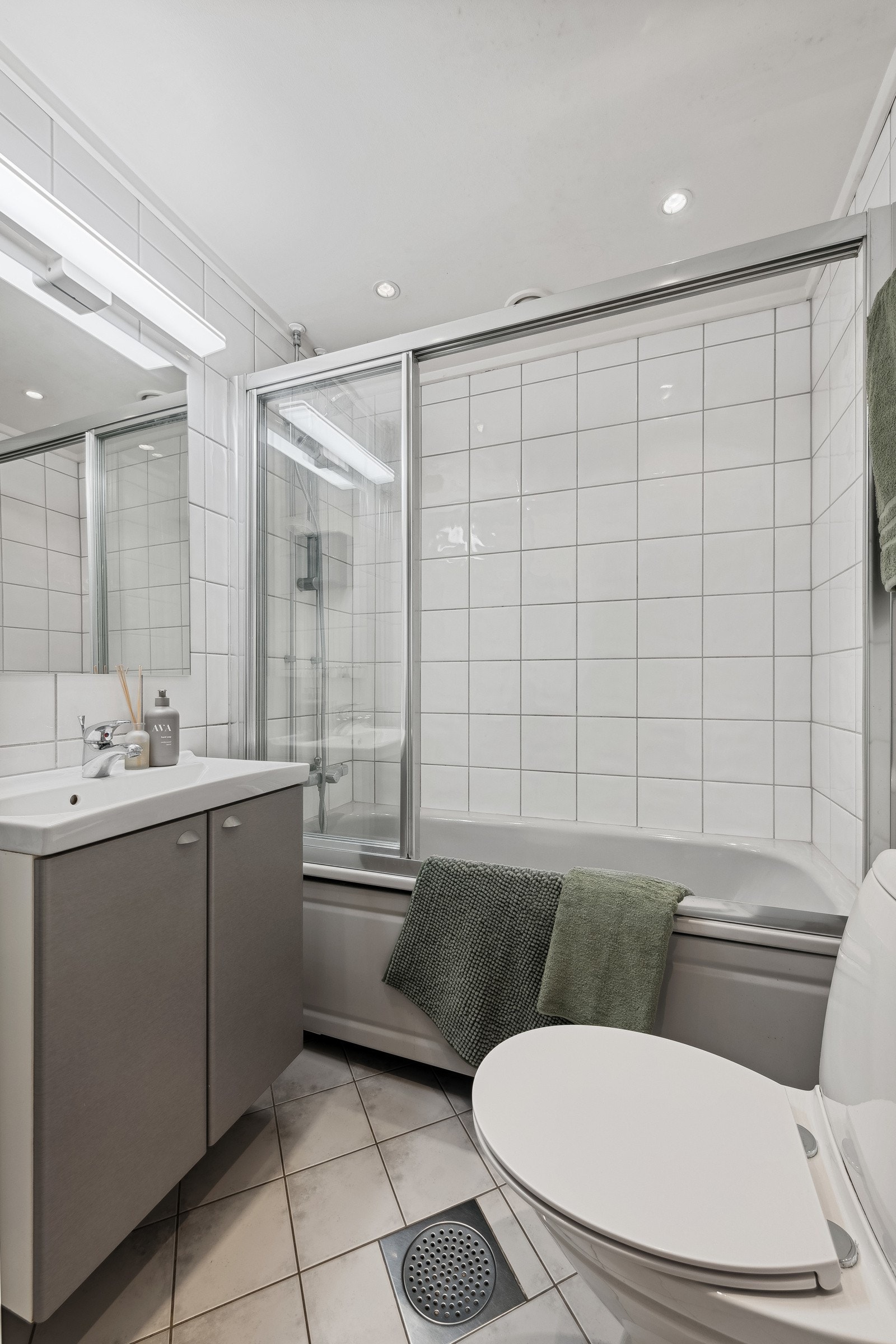 Badet er holdt i varm stil med servant nedfelt i innredning, overskap med speil i front og badekar med dusj. Varmekabler og downlights. Galleribilde