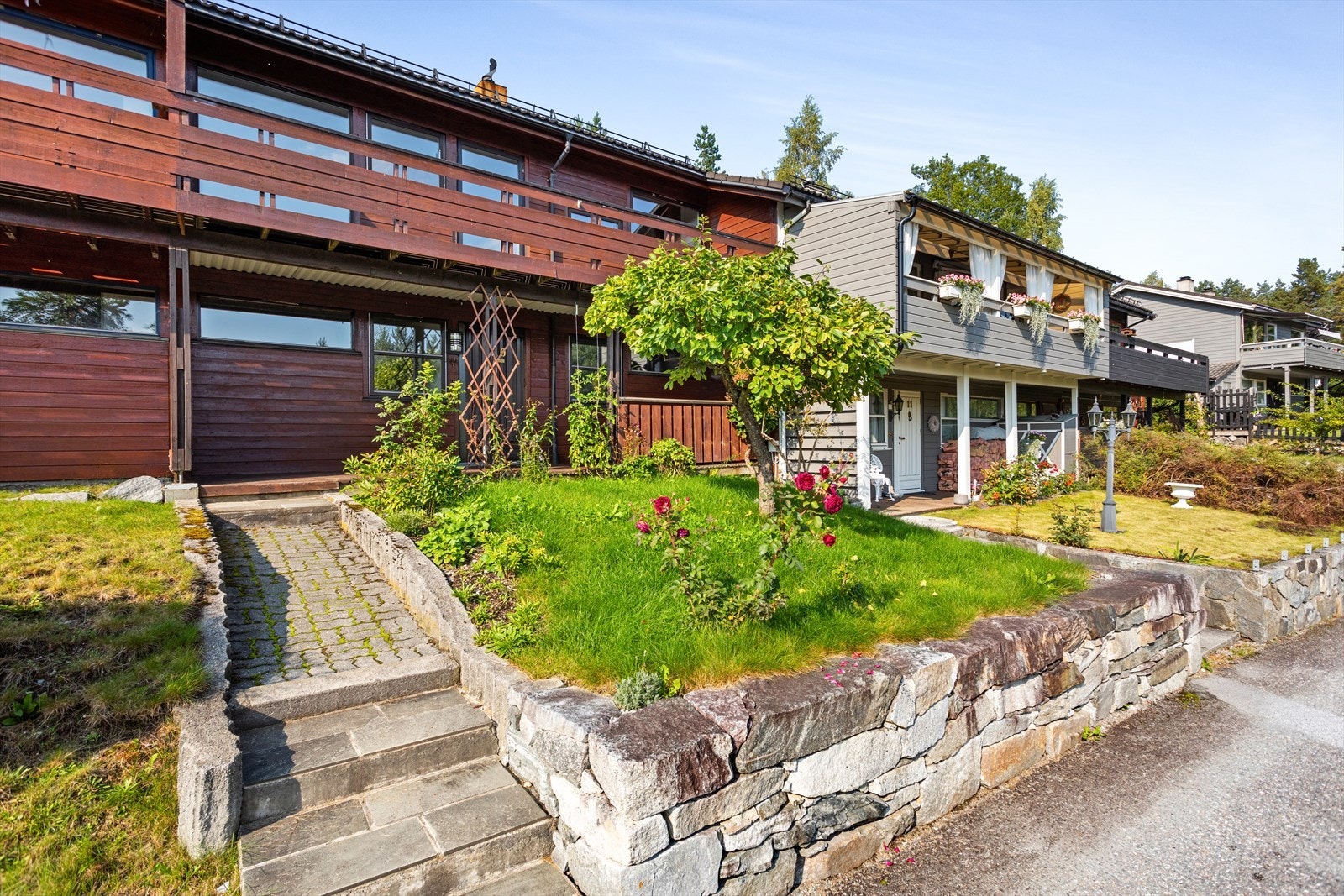 Triveleg inngangsparti med hellelagt gangareal og plenområde med beplantning. Galleribilde