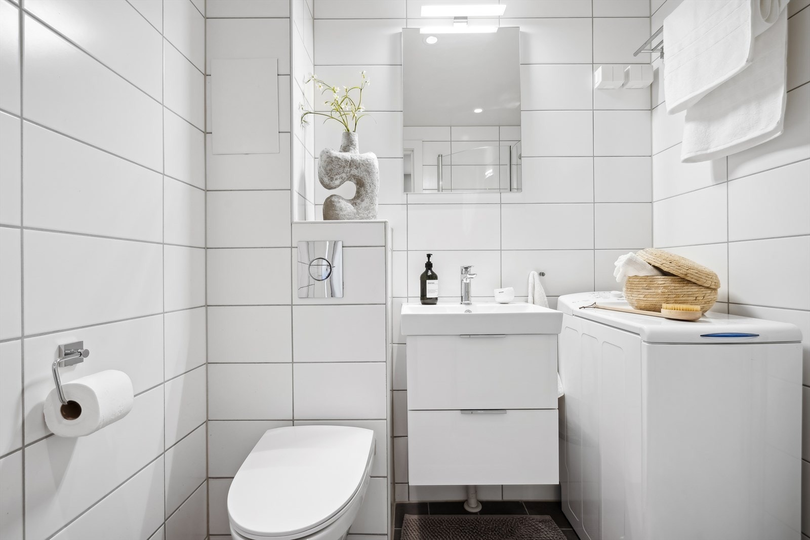 Badet er utstyrt med vegghengt toalett, dusjhjørne med glassvegg, innredning med servant og opplegg for vaskemaskin. Galleribilde