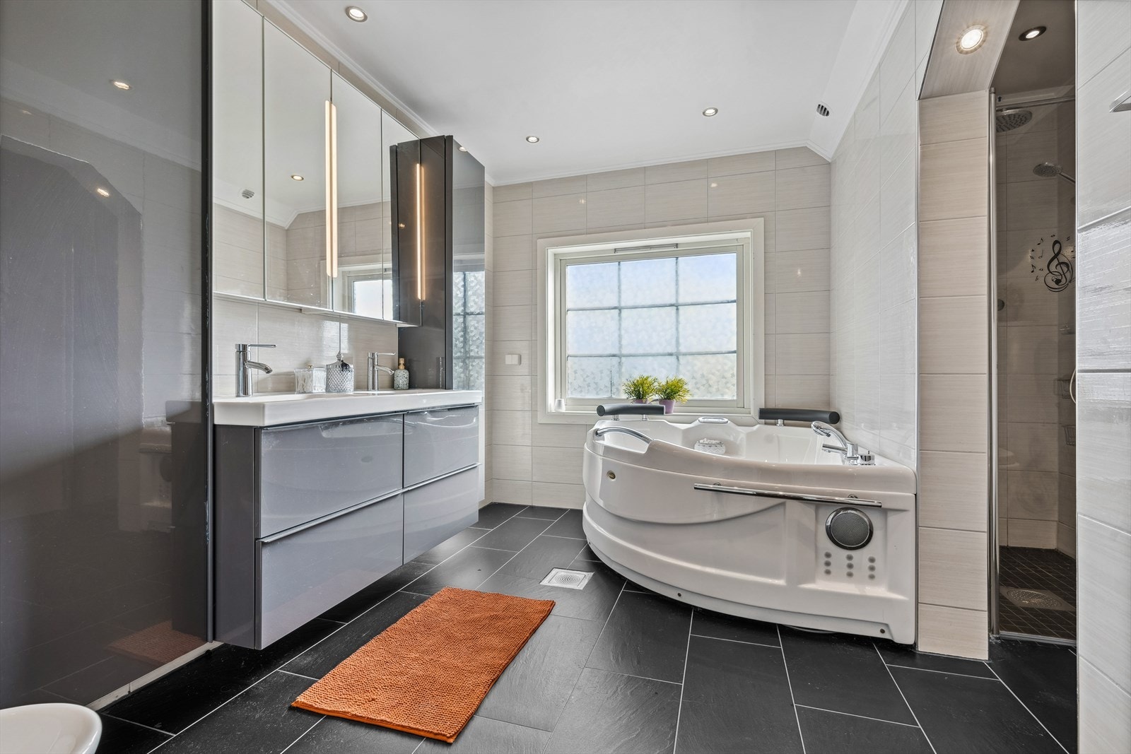 Badet er utstyrt med vegghengt toalett, bidé, dusjnisje med glassdør, boblebadekar med to-greps blandebatteri, samt stor innredning med slette fronter og heldekkende dobbelservant. Galleribilde