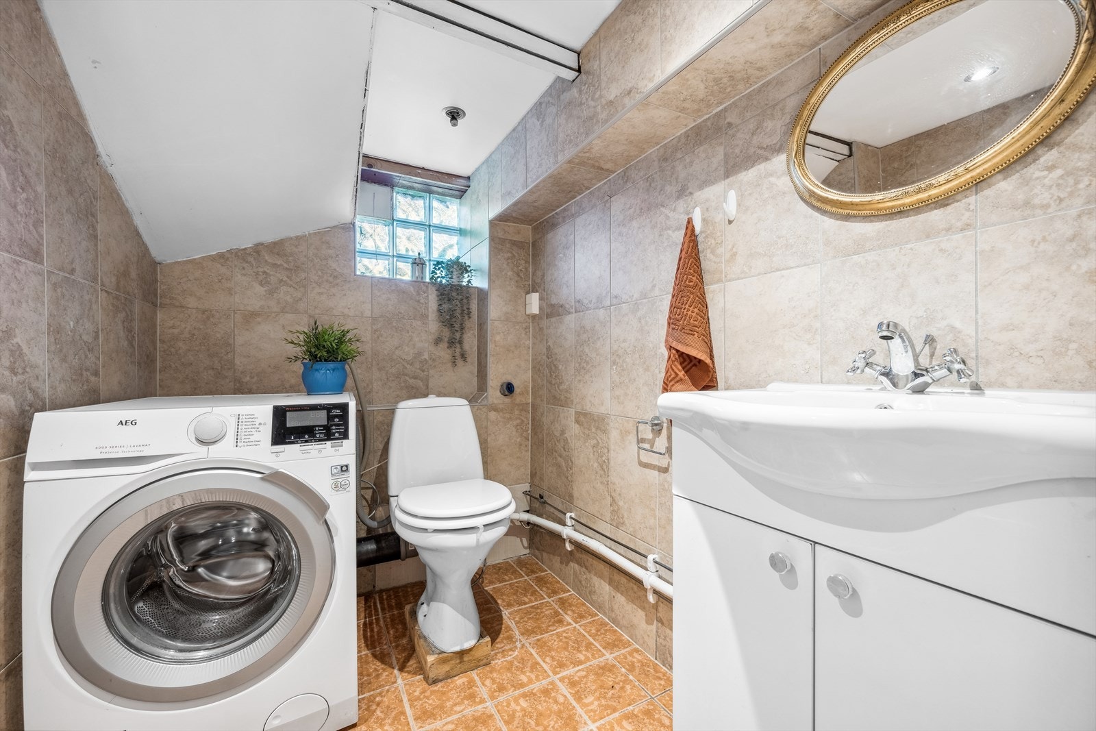 Flislagt wc innredet med toalett, servant og opplegg for vaskemaskin. Galleribilde