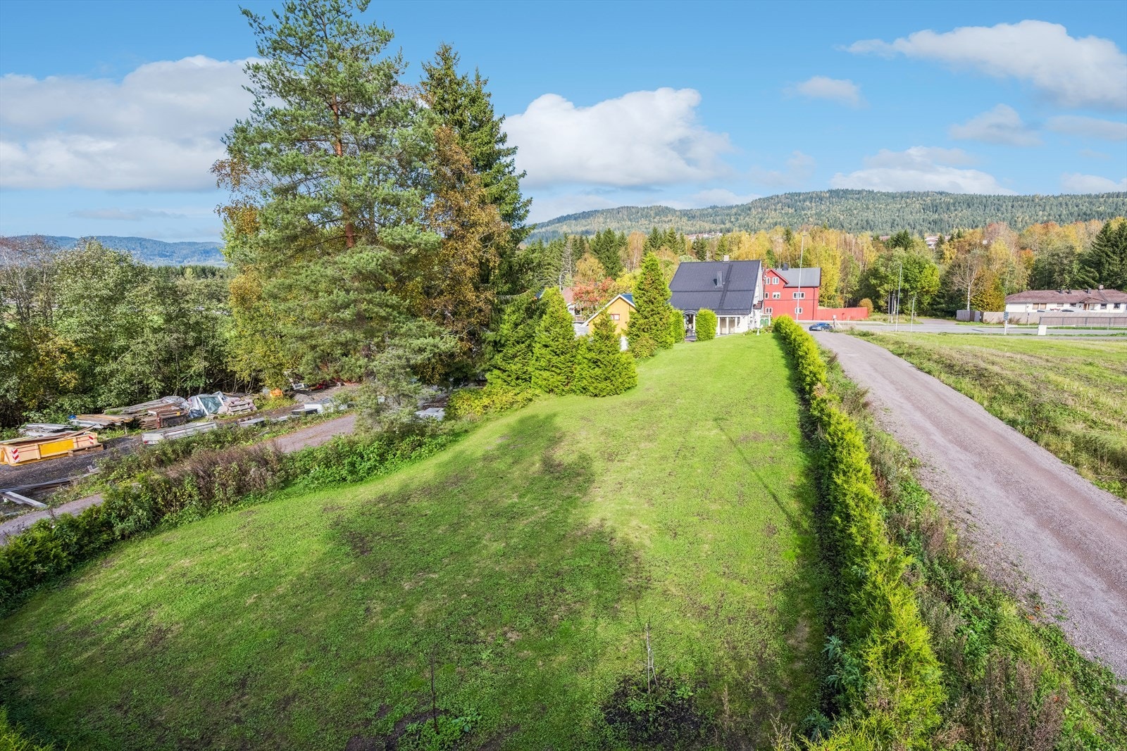 Stor skrånet tomt som er opparbeidet med gressplen, busker, hekk, uthus og terrasse. Galleribilde