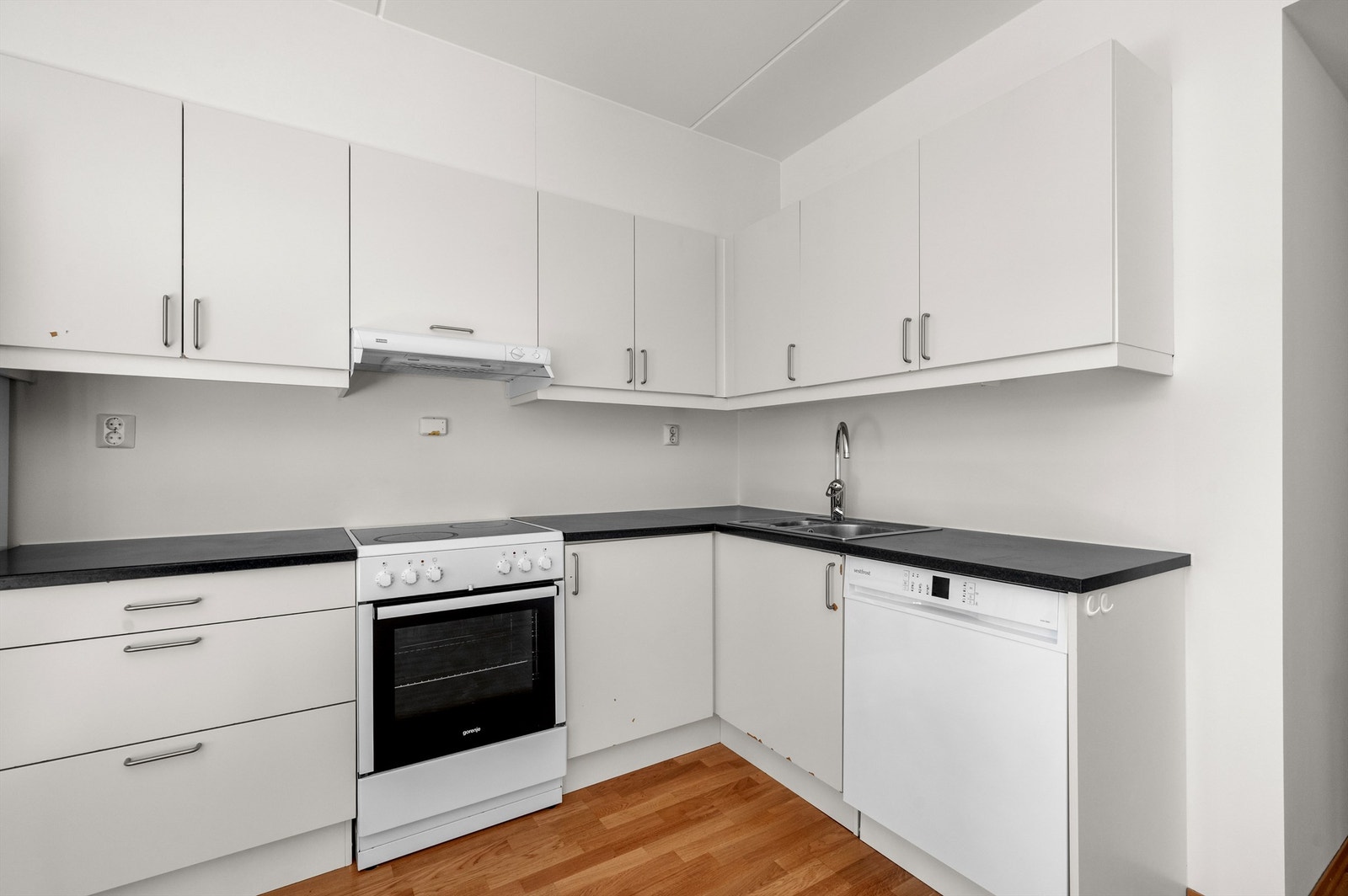 Lyst og pent kjøkken som ligger i åpen løsning med stuen. Innredningen består av hvite slette fronter, benkeplate av laminat med nedfelt oppvaskkum i rustfritt stål med ett-greps armatur. Galleribilde