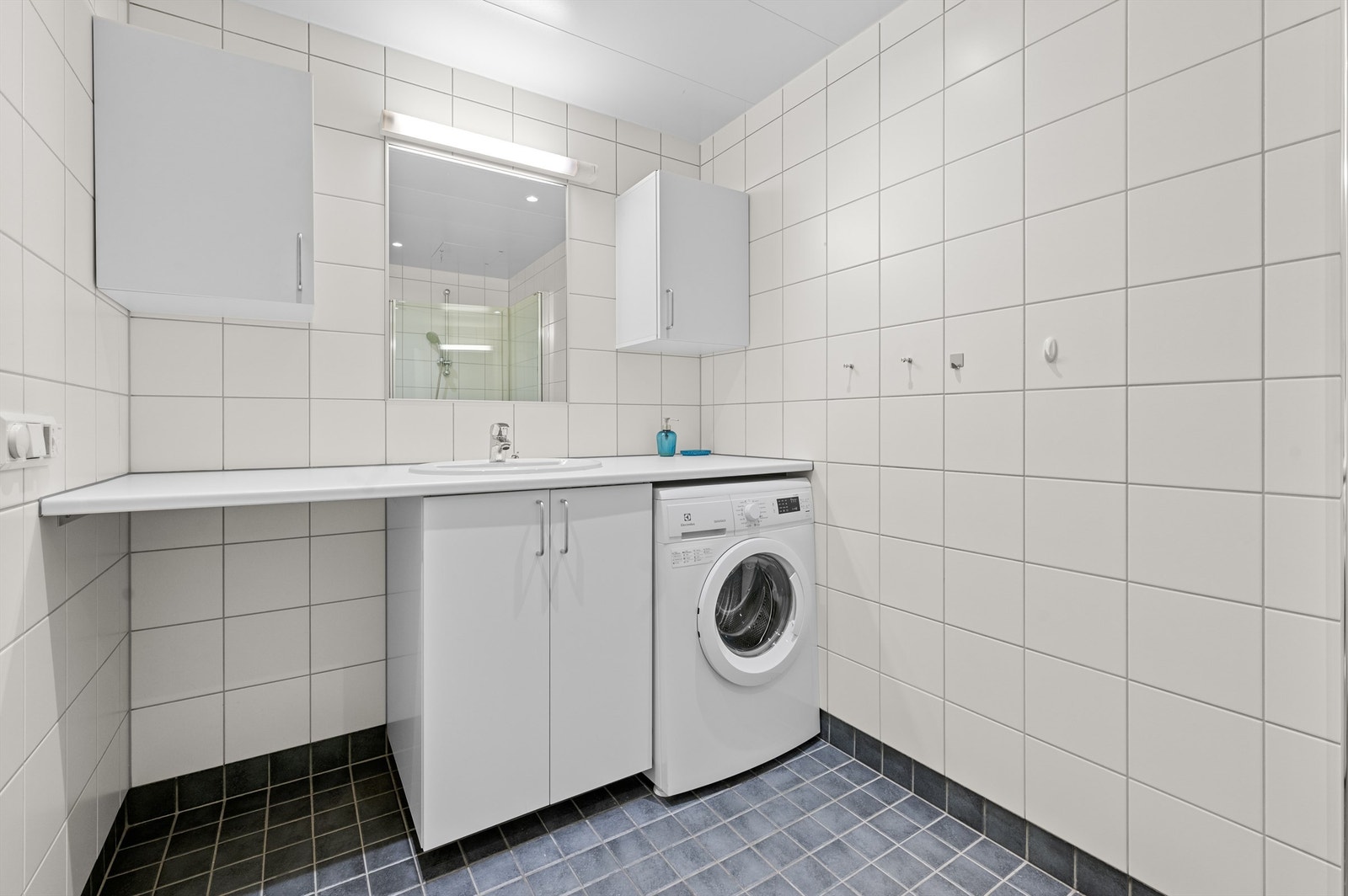 Badet har videre dusjssone med innfellbare dører av glass, og vegghengt toalett. Det er opplegg for vaskemaskin og mekanisk avtrekksventil i himling. Galleribilde