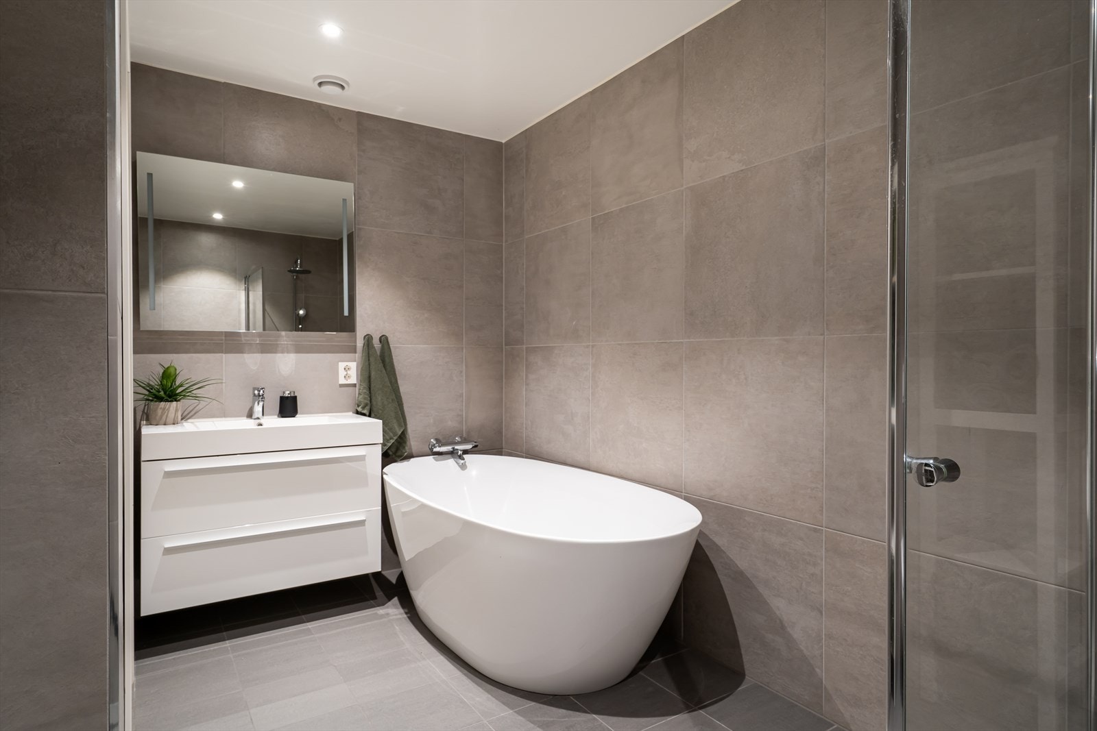 Badet holder høy standard med tidsriktige fliser, hvit innredning, overhengt speil med belysning, badekar og dusjhjørne. Galleribilde