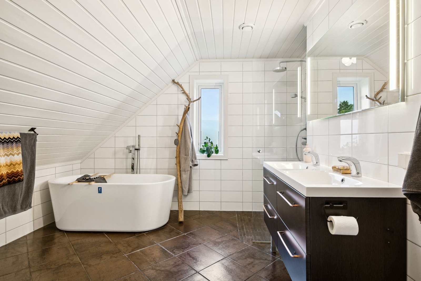 Lyst og romslig bad med skråtak, badekar og moderne servant. Perfekt for avslapning og velvære i hjemmet ditt. Galleribilde