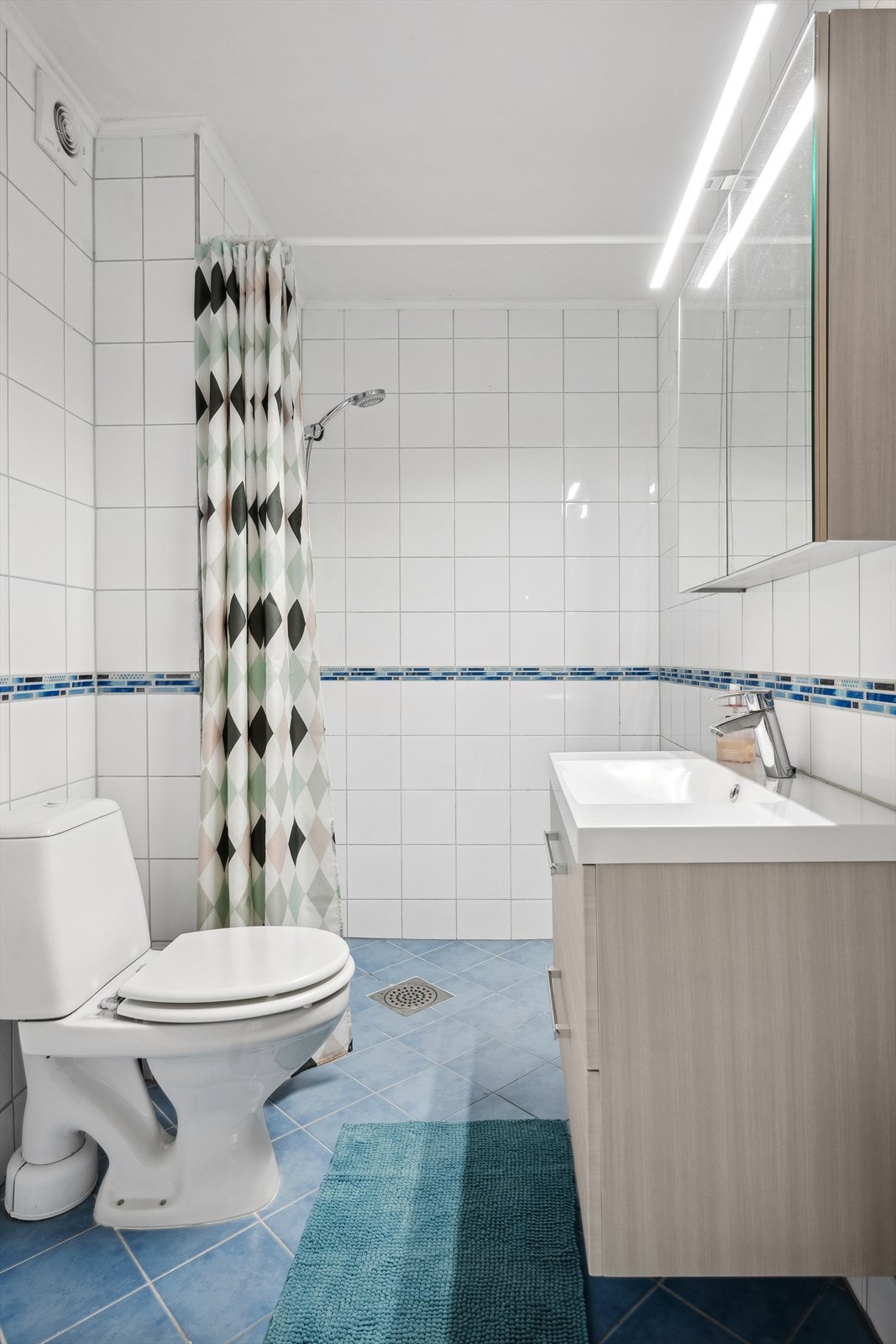 Speilskap med lysarmatur på vegg over servanten. Dusjhjørne med forheng, sluk i sone og dusjutstyr. Galleribilde