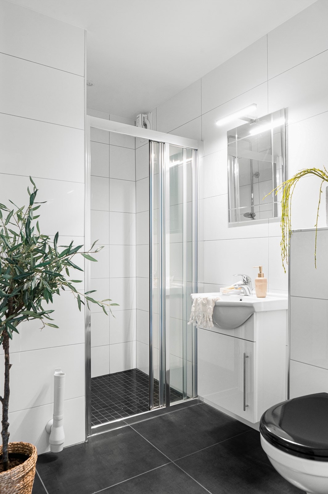 Bad 2 har et praktisk dusjhjørne, et vegghengt toalett, et speil med belysning og en plassbesparende servant med underskap. Galleribilde