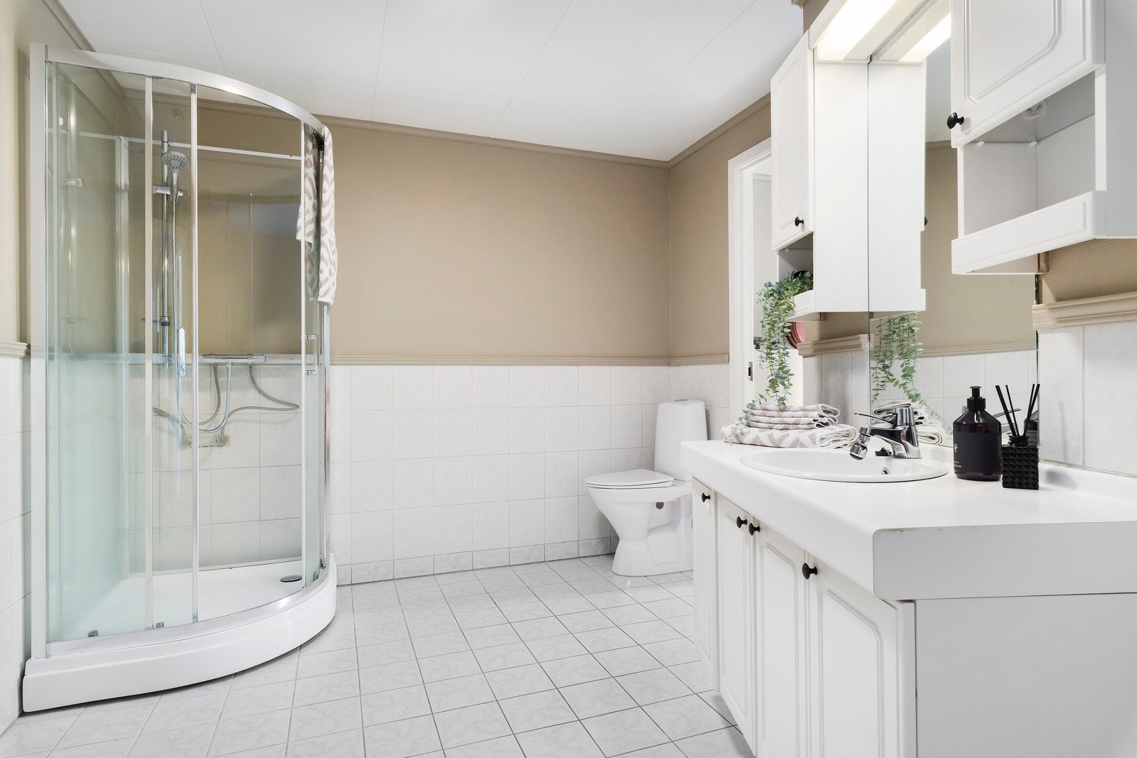 Badet har fliser på gulvet og opp langs veggen. Her er det dusjkabinett, toalett og en romslig baderomsinnredning. Galleribilde