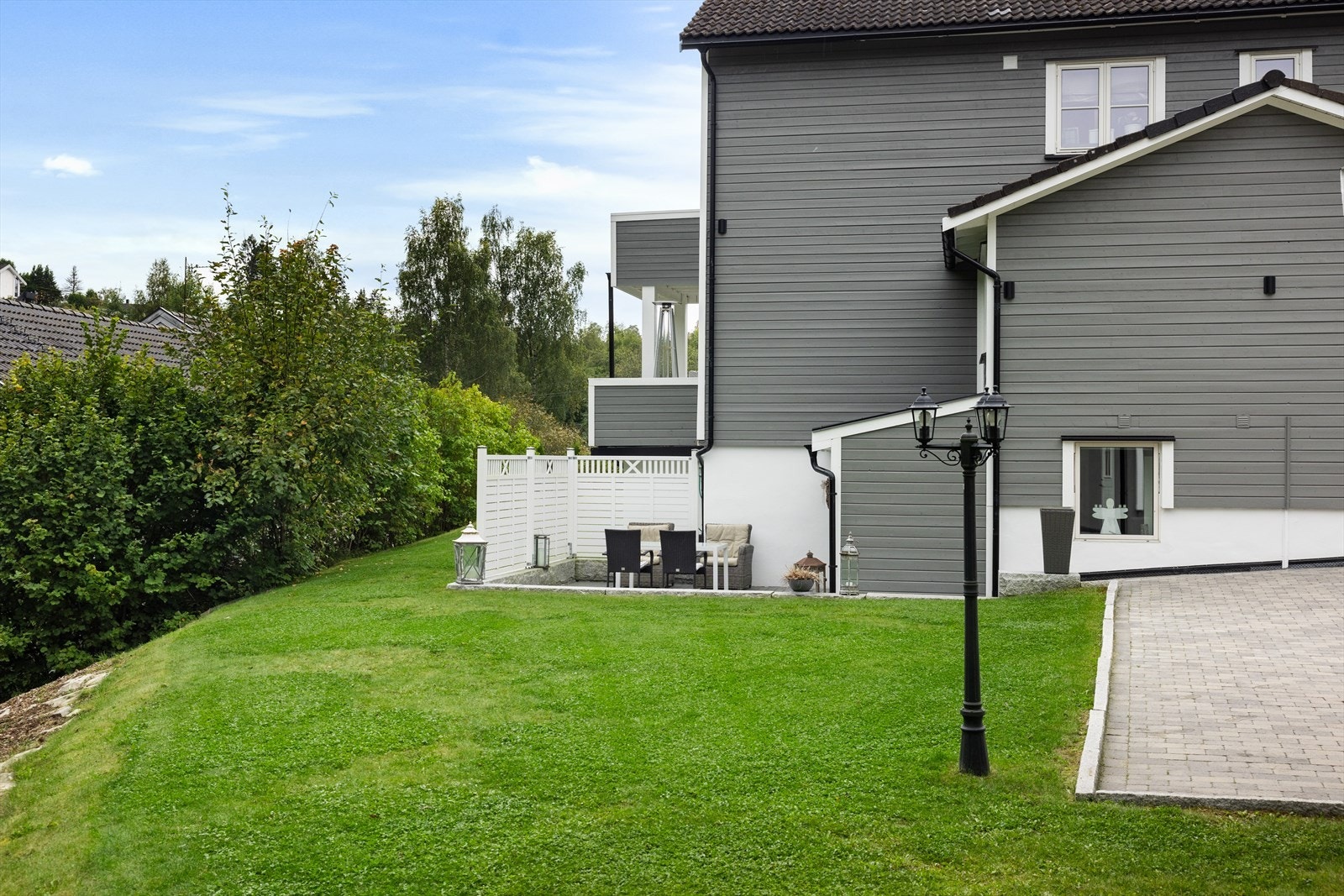 Solrik tomt med innkjørsel i asfalt og brostein. Plenareal og områder for parkering. Galleribilde
