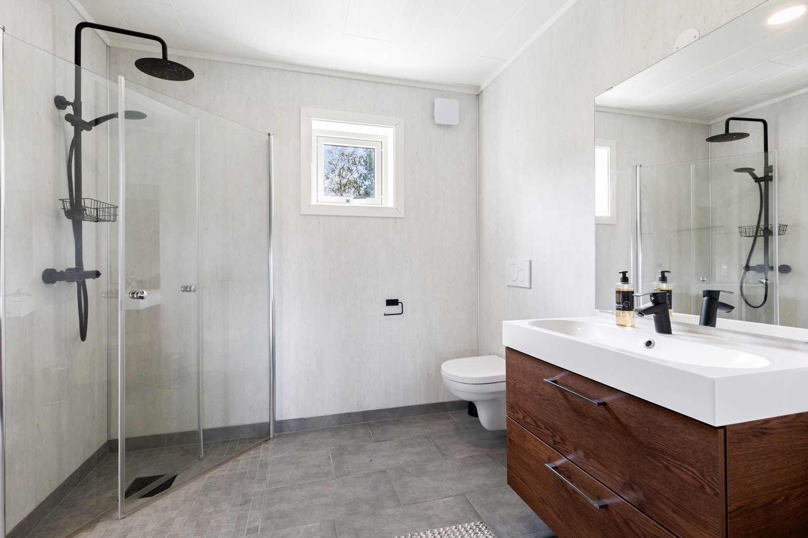 Lekkert baderom bestående av servant med underskap, vegghengt toalett og dusjhjørne med regnfalldusj - En oase av velvære. Galleribilde