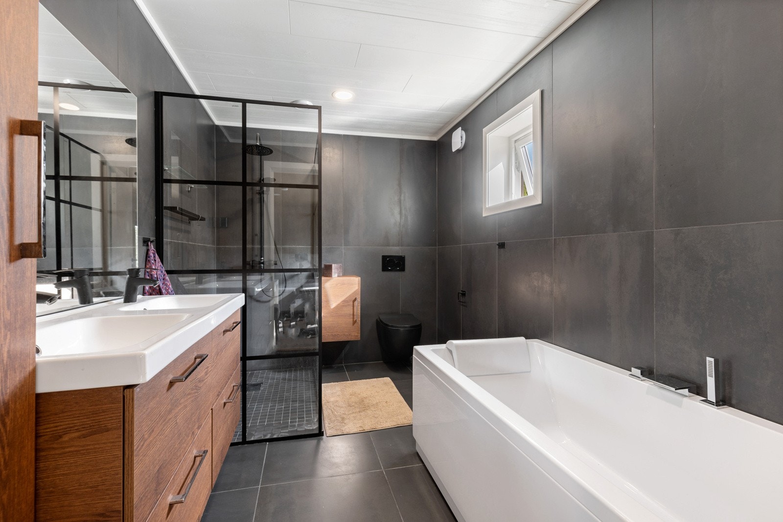 Rålekkert bad med stilrene 60x60 fliser som harmonerer godt med baderomsinnredningens jordnære farger, kombinert med badekar og moderne regndusj ? en spa-opplevelse hjemme. Galleribilde