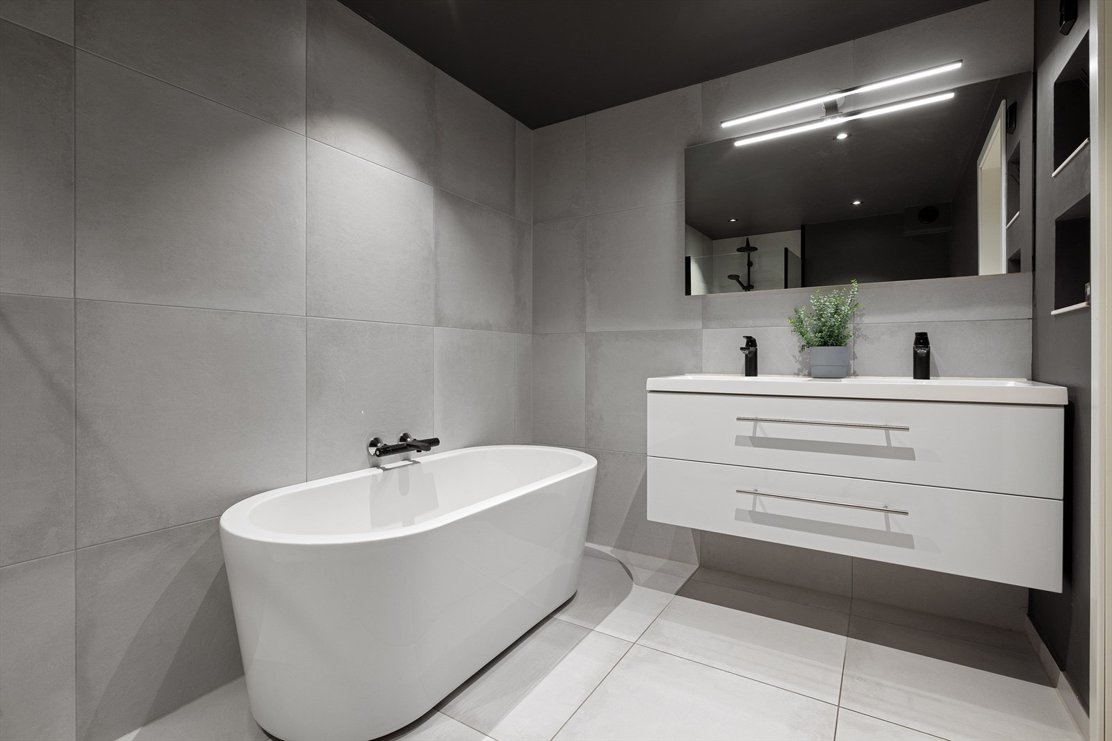 Badet er utstyrt med dusjhjørne, badekar og dobbelservant Galleribilde