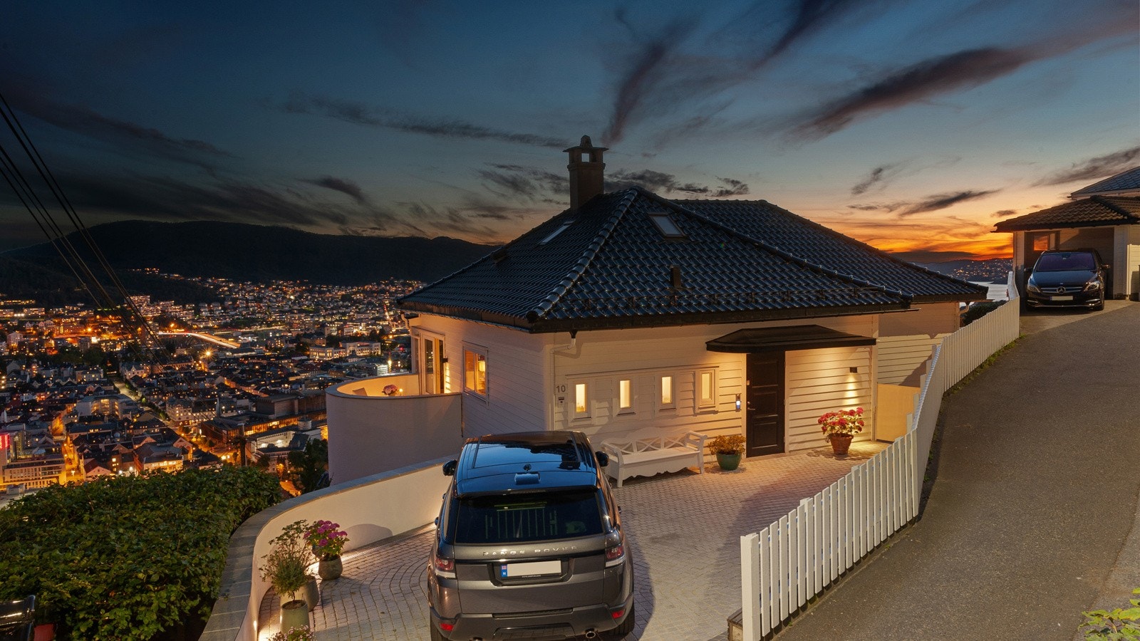 En eksepsjonell og topp utstyrt eiendom med gjennomgående HØY standard og praktfull beliggenhet i Fjellsiden. Det er tre biloppstillingsplasser på tomten inkl. en mindre garasjen i høyre billedkant. Galleribilde