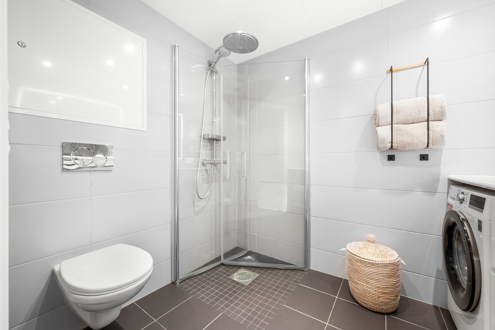 Badet er innredet med vegghengt toalett, dusjhjørne med svingbare glassdører og baderomsinnredning med servant nedfelt i innredning Galleribilde