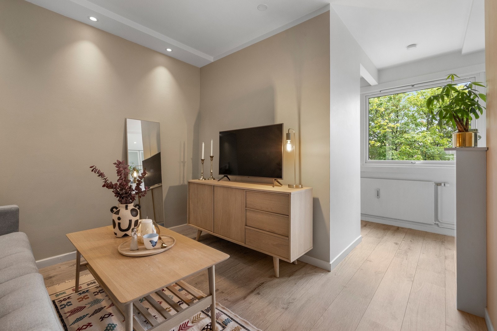 Leiligheten har en meget pen stue med enstavs laminat på gulv, harmonisk farge på vegger og downlights Galleribilde