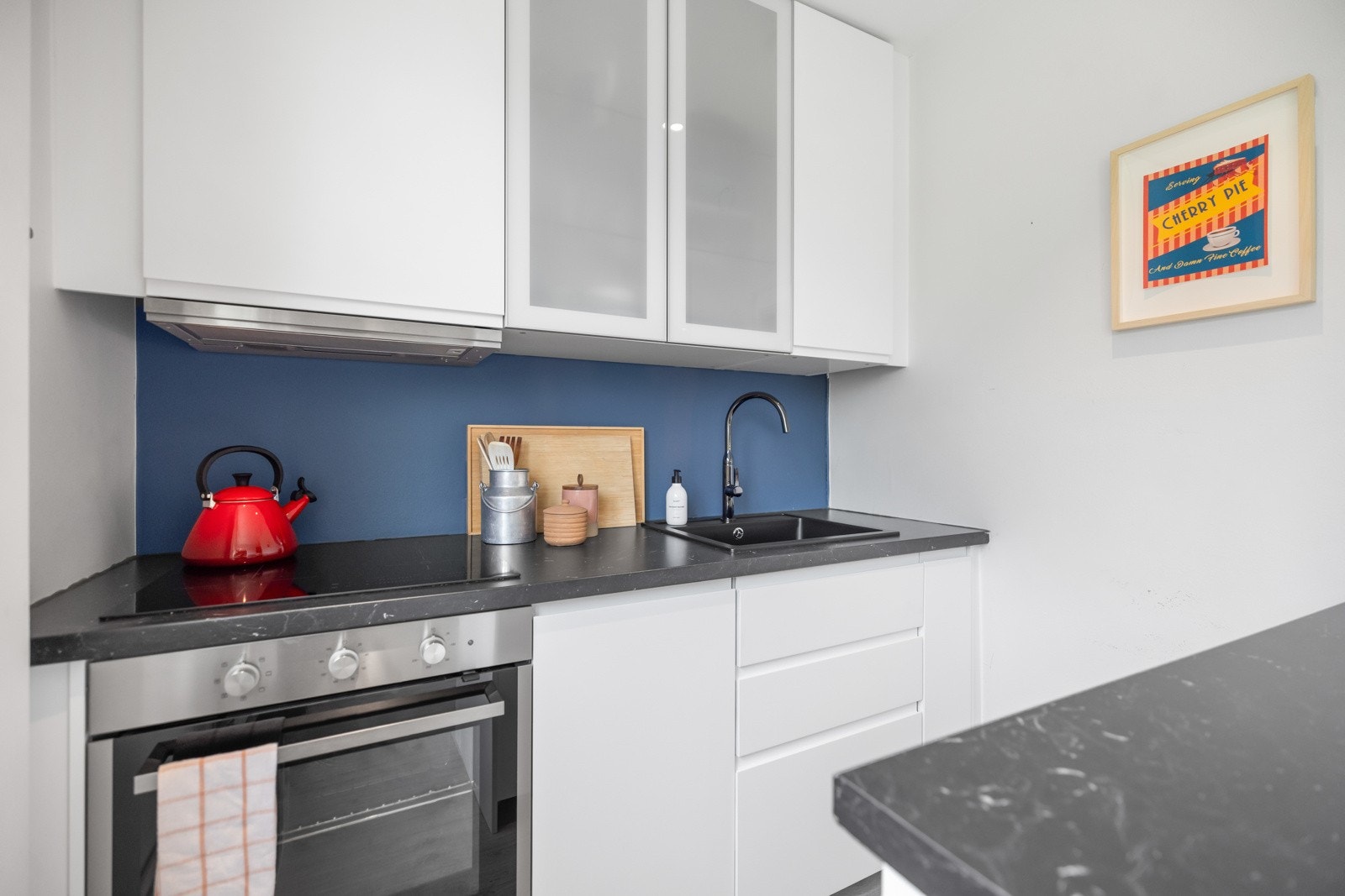 Innredningen er hvit med glatte fronter, frostede vitrineskap, benkeplate av laminat og mørk oppvaskkum Galleribilde