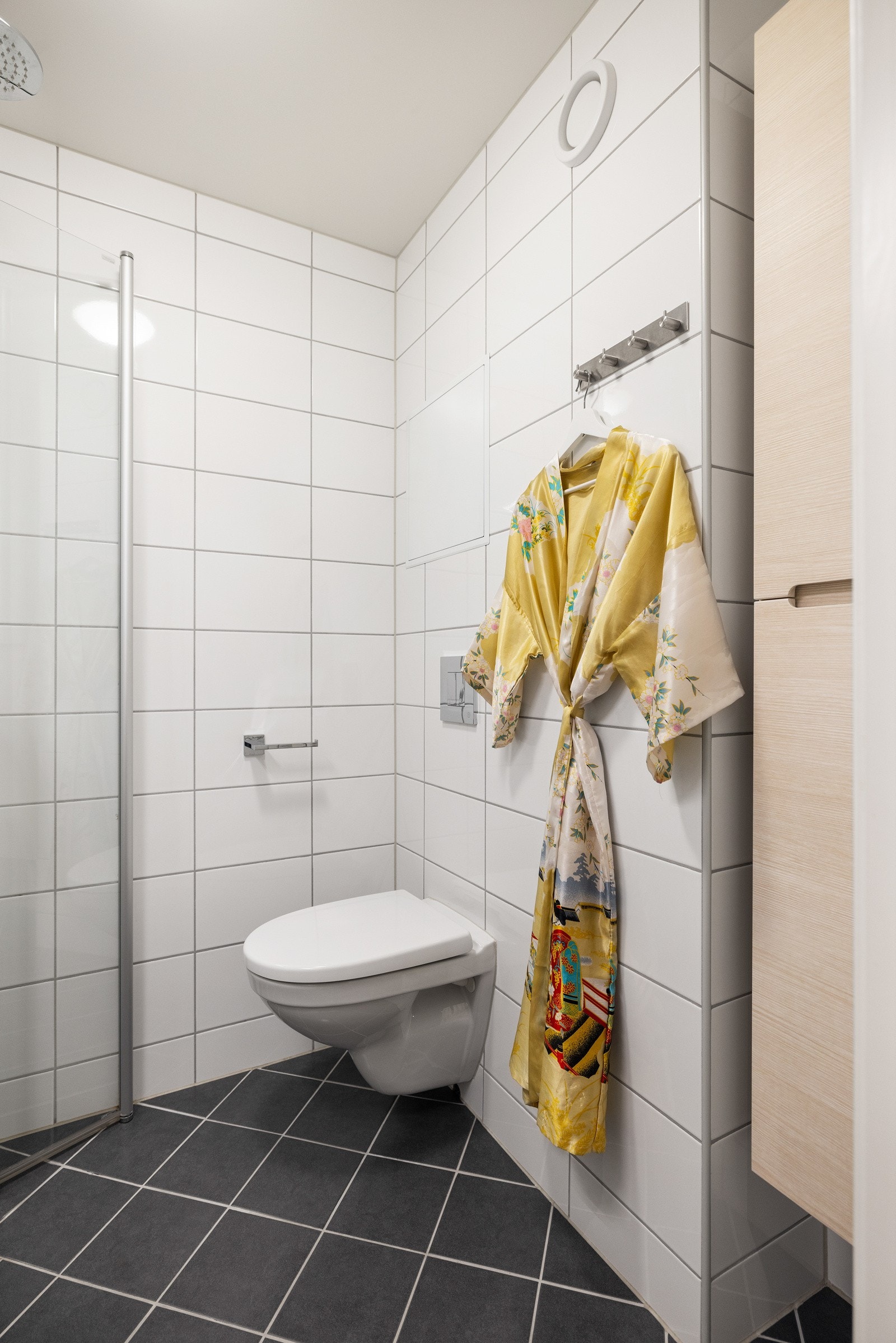 Badet har veggmontert toalett, samt dusjhjørne med både håndgarnityr og regnfallsdusj Galleribilde