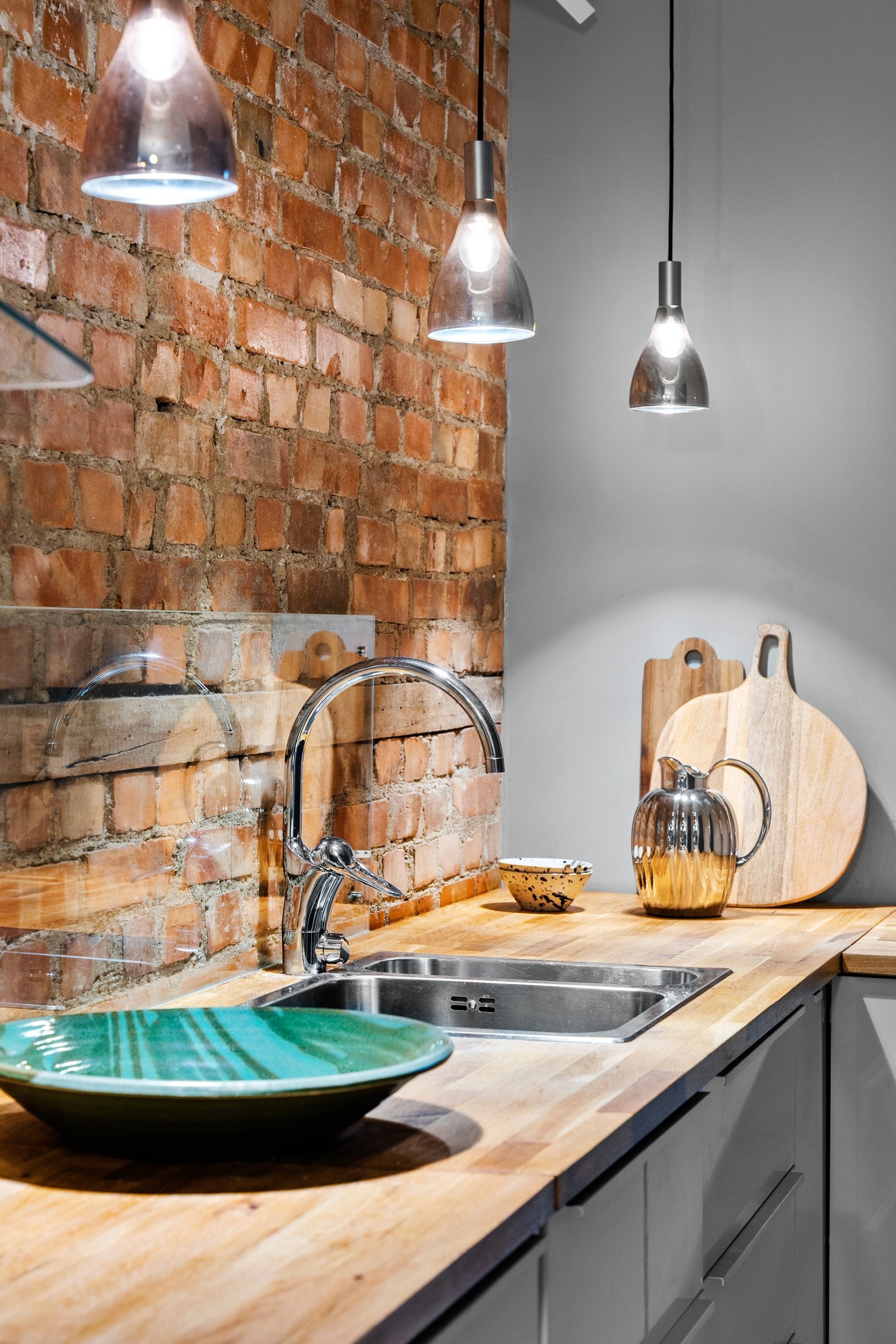 En bakvegg i original teglstein gir en industriell look, og over benken er det montert god arbeidsbelysning i form av pendellamper Galleribilde