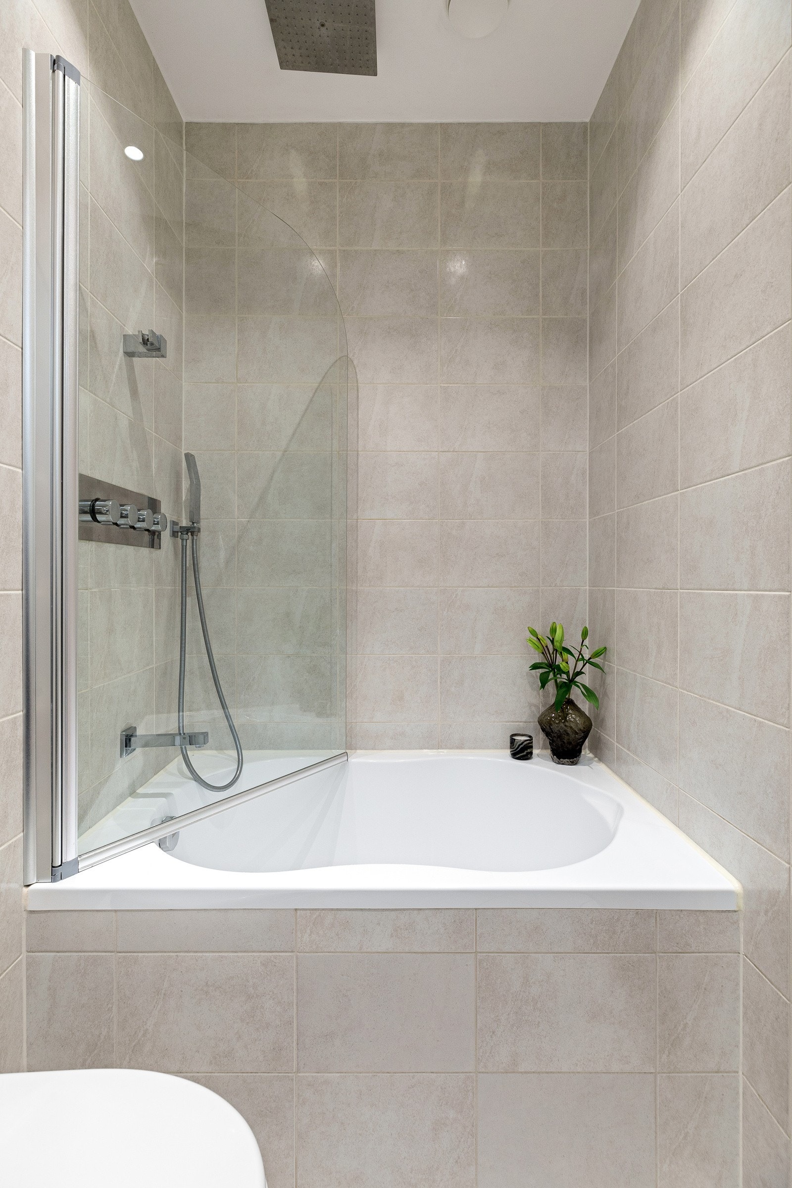 Badet består av innmurt badekar med glassvegg og regnfalldusj, veggmontert servantskap, speilskap og vegghengt toalett Galleribilde