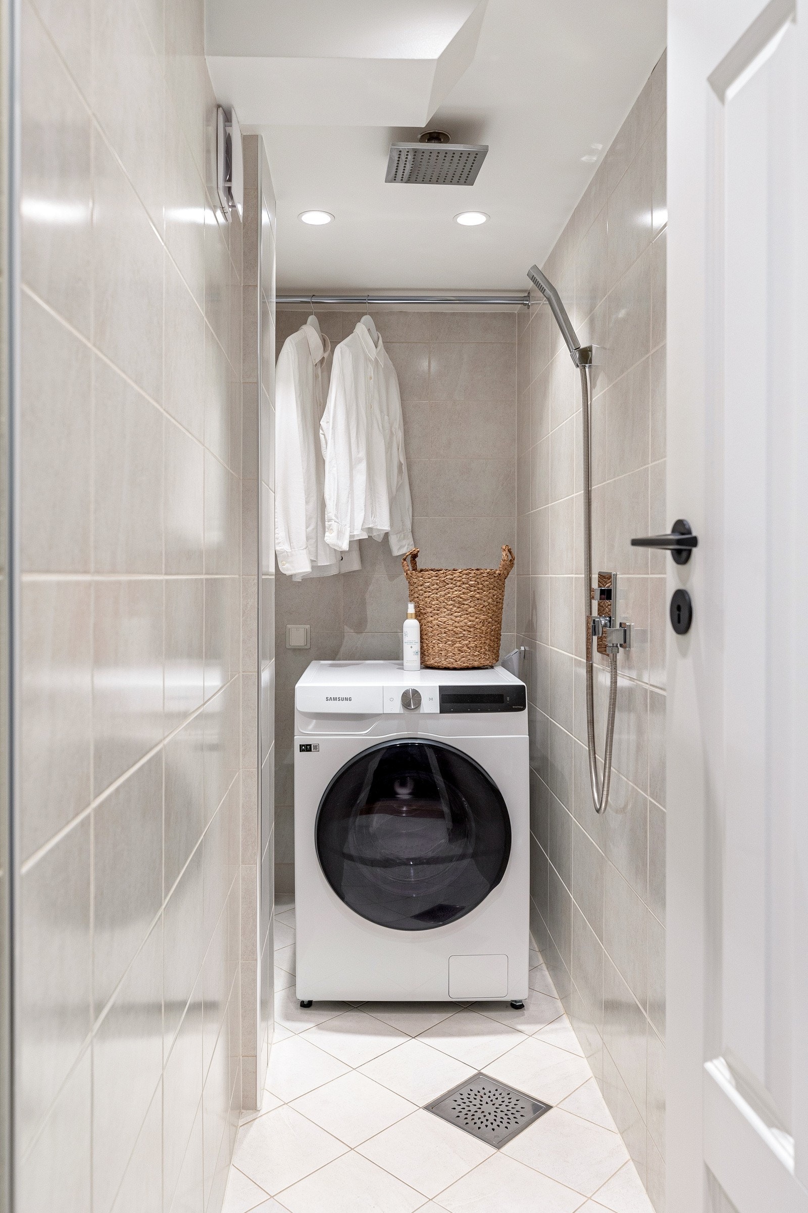 Flislagt vaskerom med varmekabler i gulv, regnfall- og hånddusj og opplegg for vaskemaskin. Over vaskemaskinen er det montert en praktisk stang for tørk av klær Galleribilde