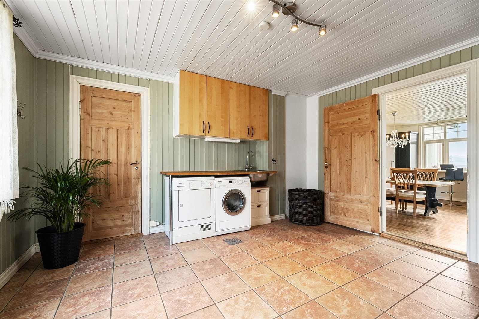 Romslig vaskerom har flislagt gulv med gulvvarme, panel på vegg, med opplegg til vaskemaskin, skyllekar og innredning/skap Galleribilde