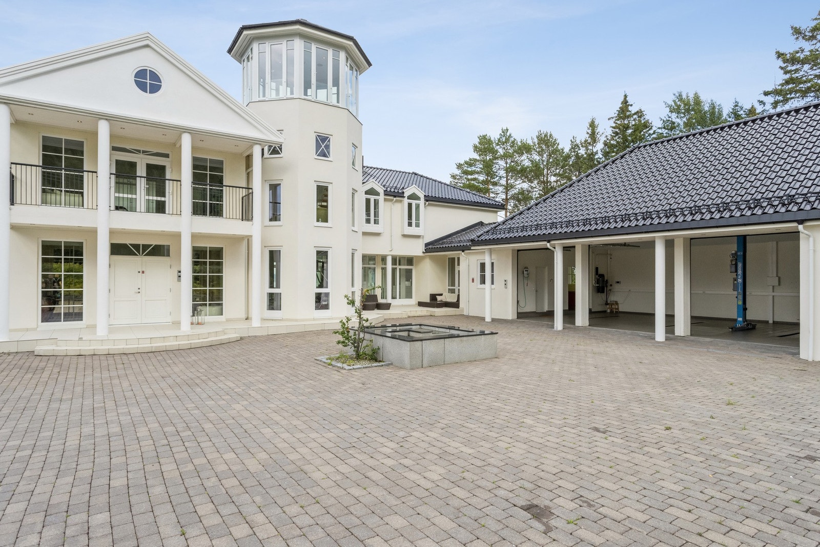Stor steinbelagt gårdsplass med trippelgarasje og flere oppstillingsplasser. Derav en med elbil-lader. Galleribilde