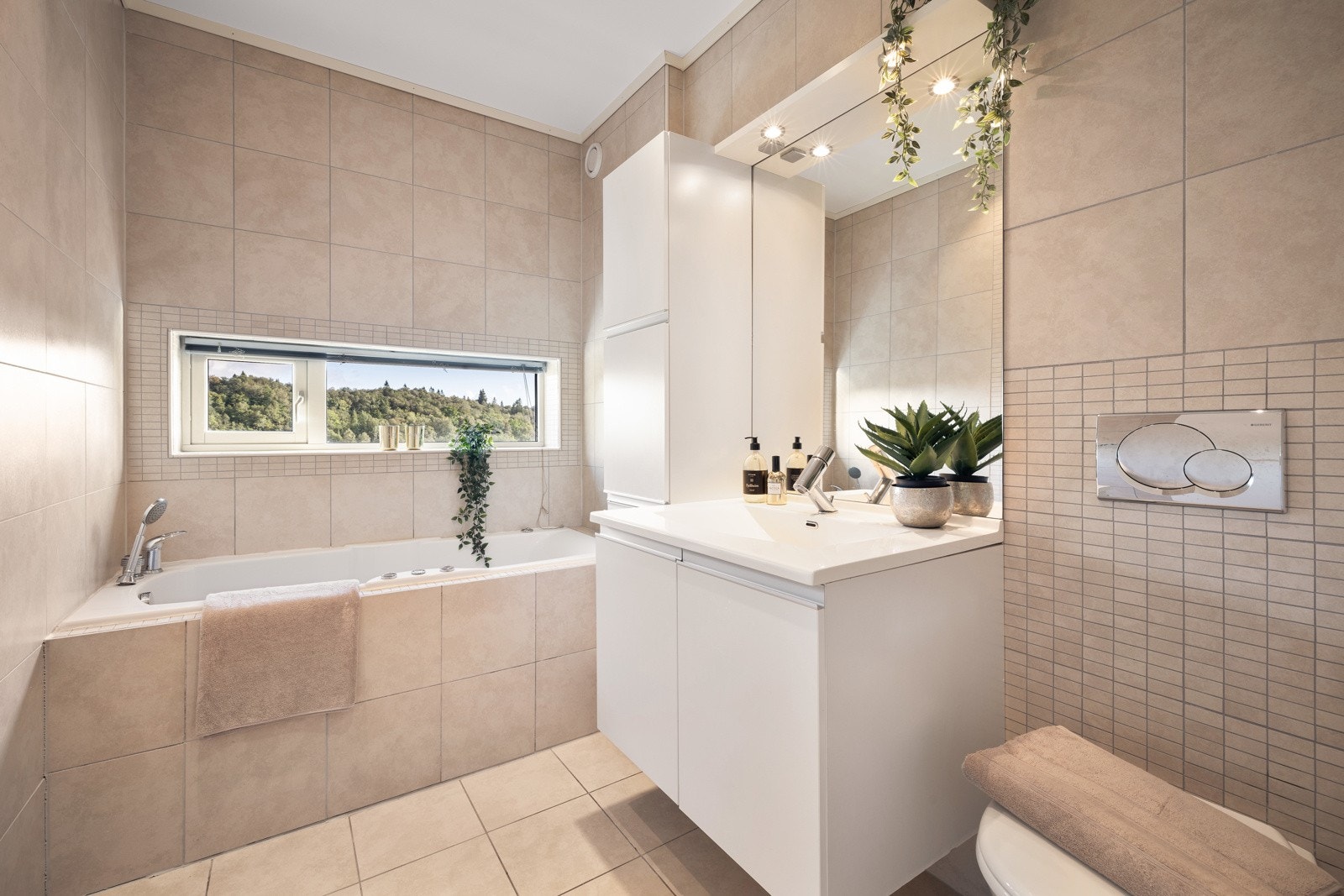 Badet er pent innredet med inn-fliset badekar, helstøpt servant med møbel, vegghengt skap og vegghengt toalett. Galleribilde