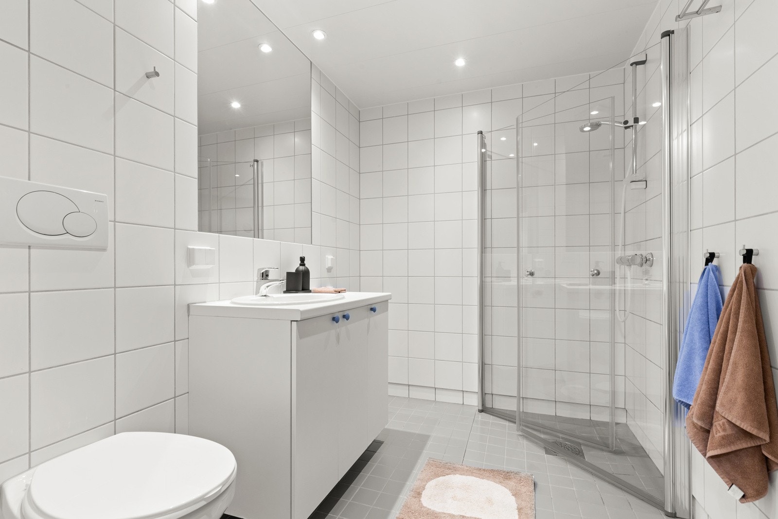Badet er utstyrt med dusj med innfellbare glassvegger, servantseksjon med skap og nedfelt porselensvask, innmurt speil, vegghengt wc og opplegg for vaskemaskin/tørketrommel. Galleribilde