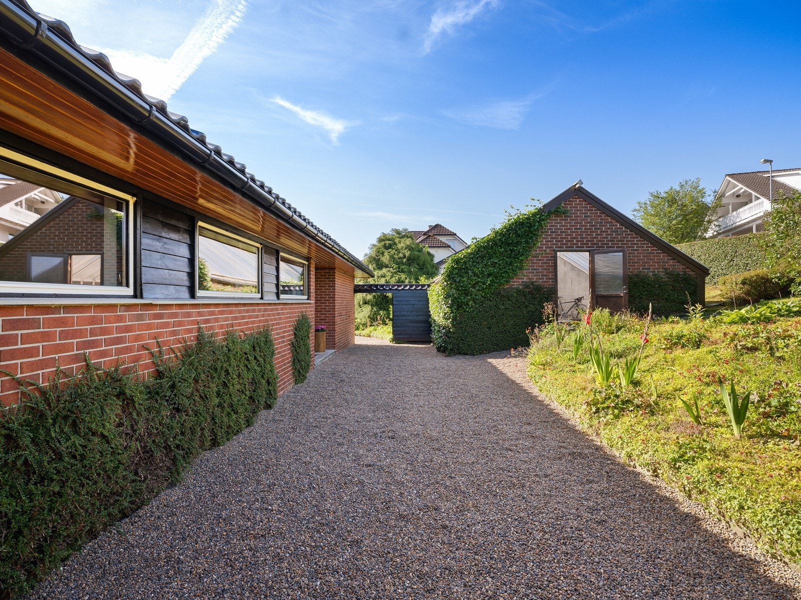 Uteområde på forsiden av boligen er opparbeidet med bed, hekk ut mot veien og et stort drivhus. Galleribilde