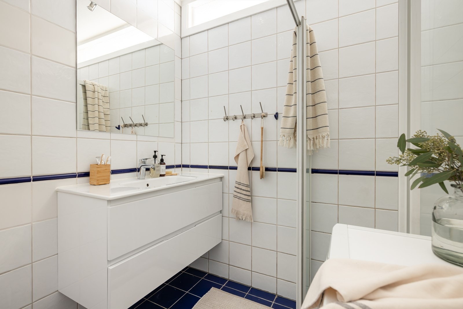 Badet er innredet med hel servantplate med servantskap, toalett, hjørnedusj med glassvegger/dører og fast gulvskinne. Galleribilde