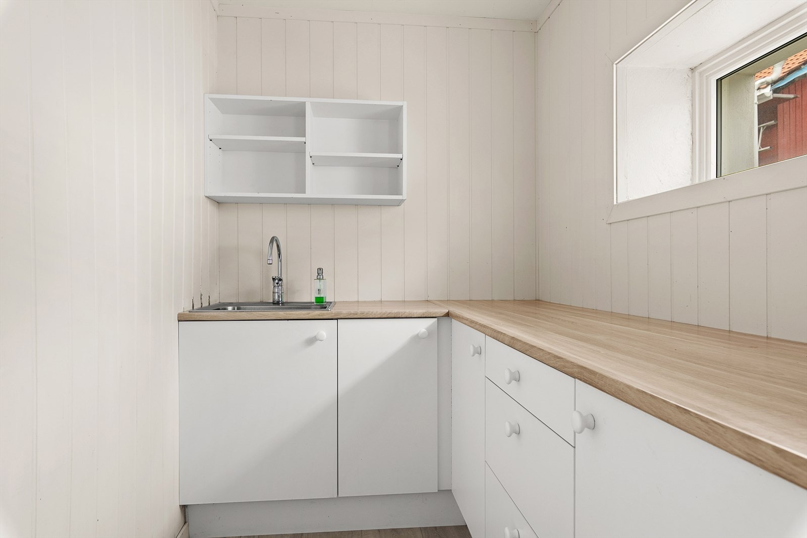 Kjøkken med enkel innredning med hvite fronter og laminat benkeplate. Integrert koketopp og stekeovn. Galleribilde