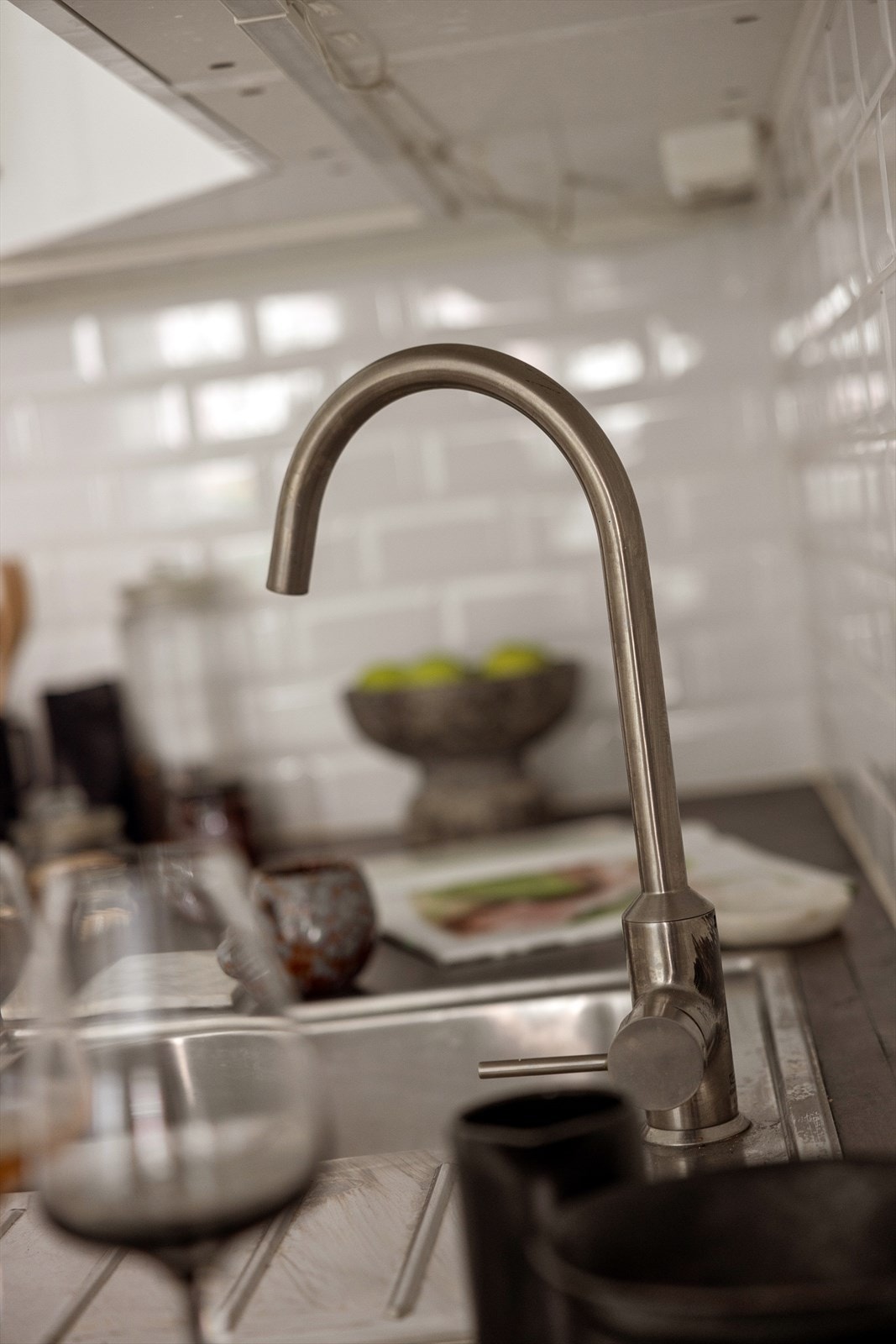 Kjøkkenet har glatte høyglansfolierte fronter, vitrinedører med frostet glass, og en rustfri kum nedfelt i en heltre benkeplate. Galleribilde