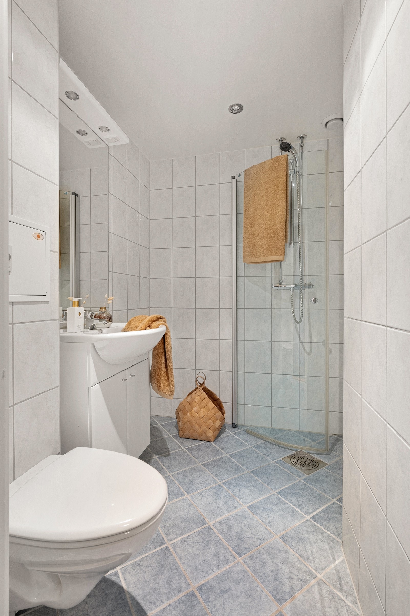 Badet er utstyrt med dusjhjørne med to svingbare glassdører og togreps blandebatteri, slett innredning med heldekkende servant med ettgreps blandebatteri og vegghengt toalett. Galleribilde