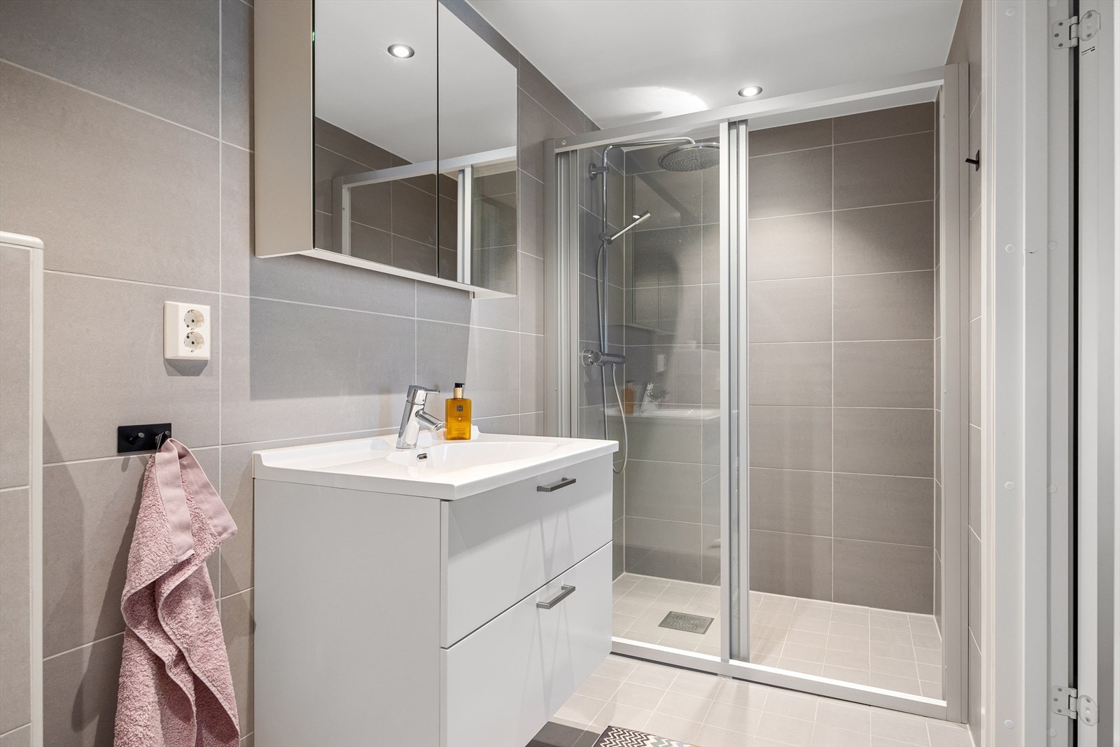 Badet består av servant, skap, speil med belysning, veggmontert toalett og dusjhjørne med vegg/dør i herdet glass. Galleribilde