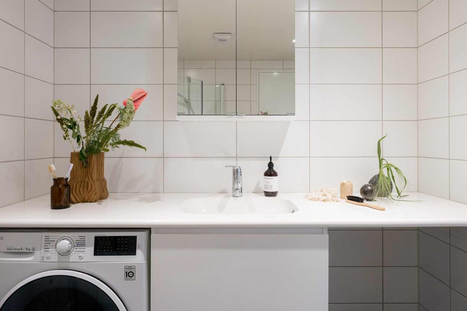 Et delikat baderom med opplegg for vaskemaskin og tørketrommel under en pen benkeplate som gir oppbevaringsplass. Galleribilde