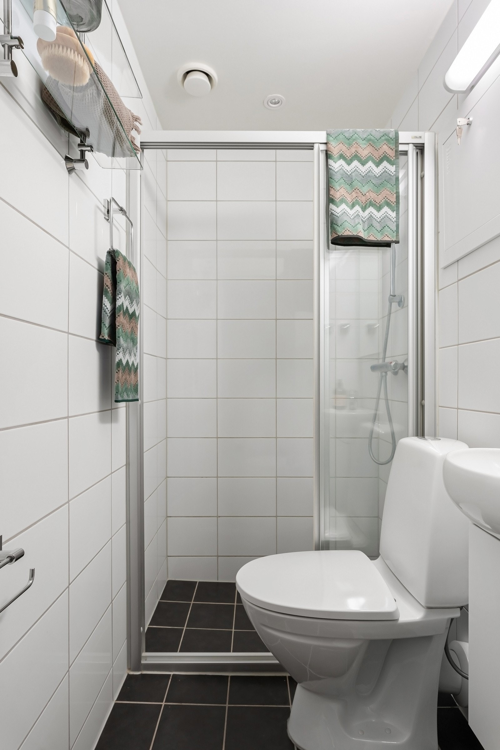 Fint, flislagt baderom som består av dusjhjørne, toalett, servant over innredning og speil. Galleribilde