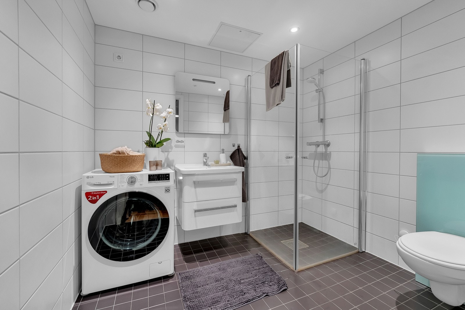 Pent bad med moderne fliser, dusj, toalett og opplegg for vaskemaskin og tørketrommel. Galleribilde